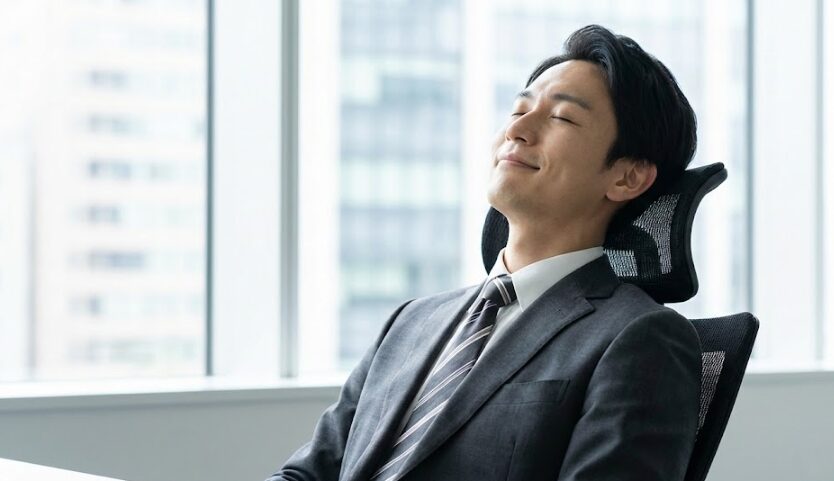 ワークチェアの大型ヘッドレストに頭を預け、リラックスして思考に耽るビジネスマン。