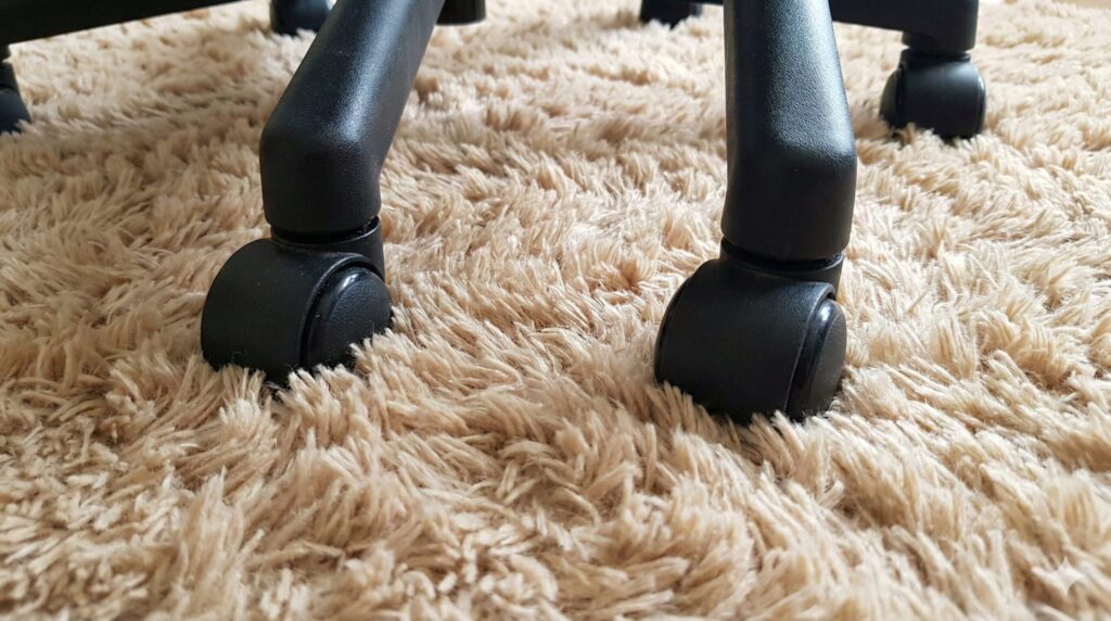 毛足の長いふかふかのラグに、オフィスチェアの黒いキャスターが深く沈み込んでおり、移動が困難な状態を示しているクローズアップ写真。